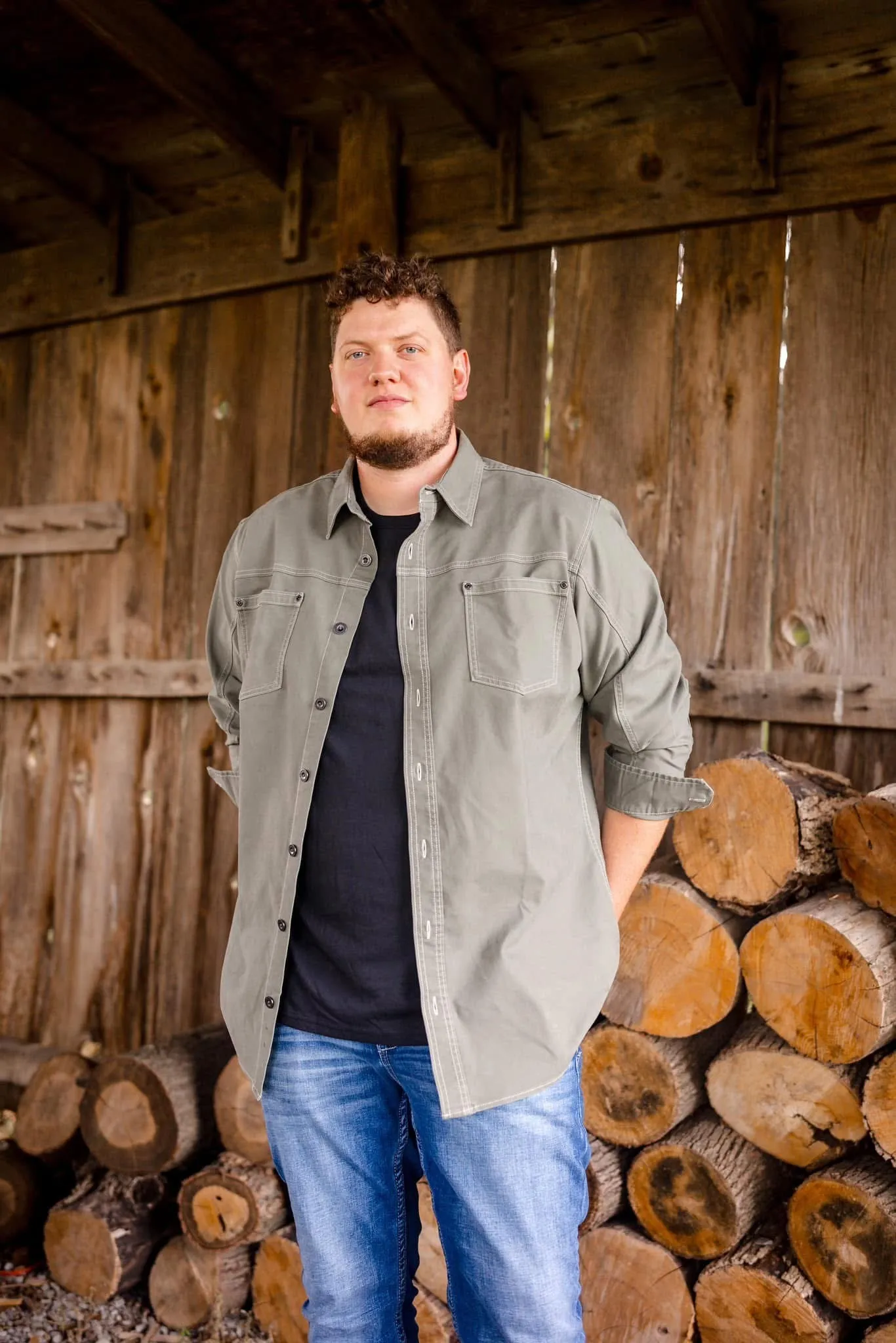 Isaac Buschur standing in front of stacked firewood
